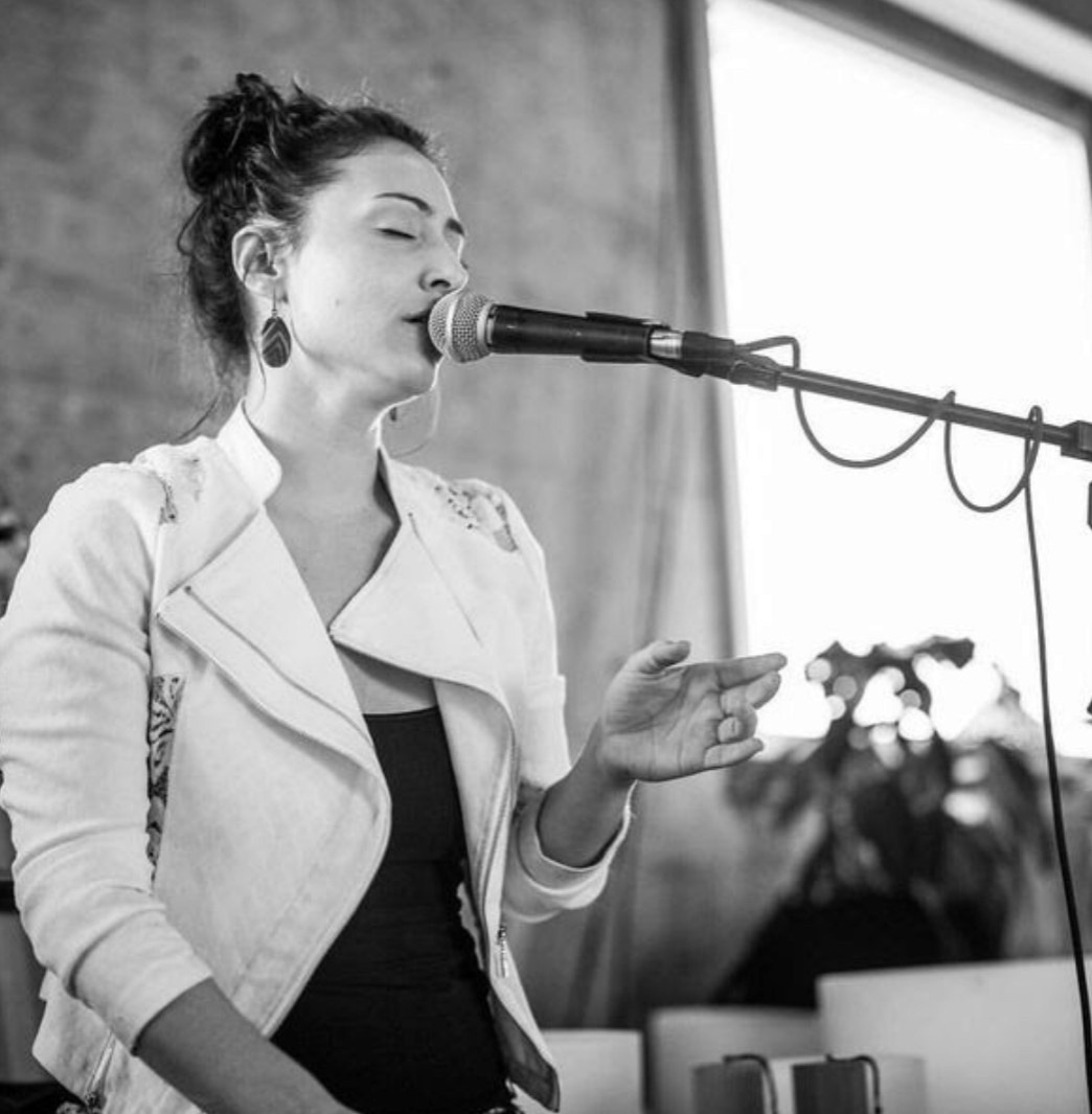 Larisa singing into a microphone with her eyes closed, fully present in her voice